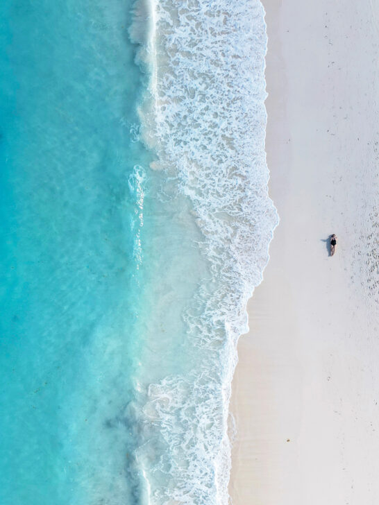 woman laying on beach drone photo with white wave and blue ocean from above