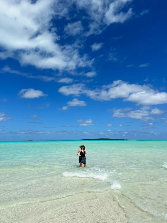 woman standing in water on sandbar in teal water and blue sky in Big Exuma Bahamas