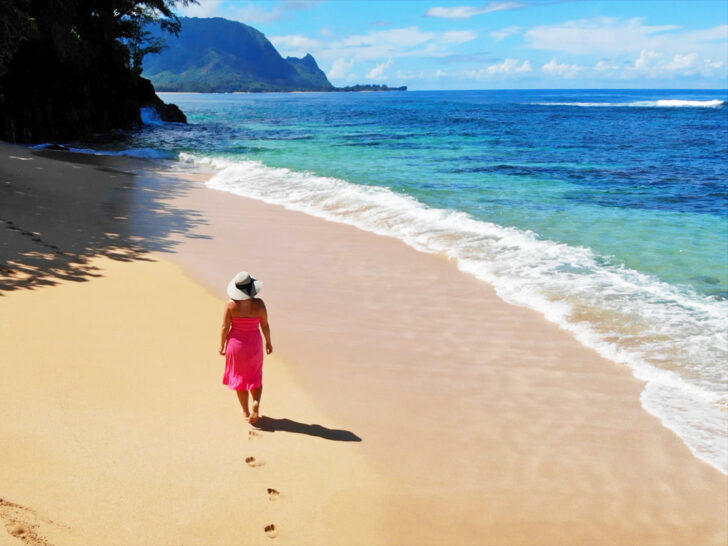 kauai drone photos woman walking in pink dress with sun hat on beach in kauai hawaii