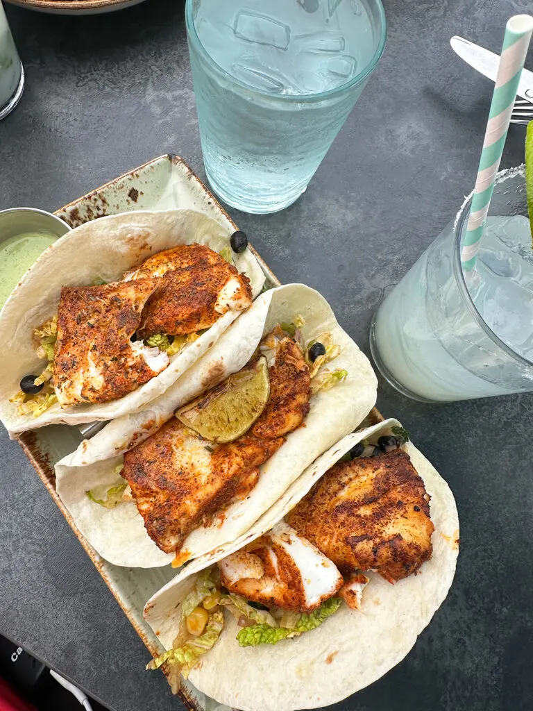 three fish tacos with glasses on table