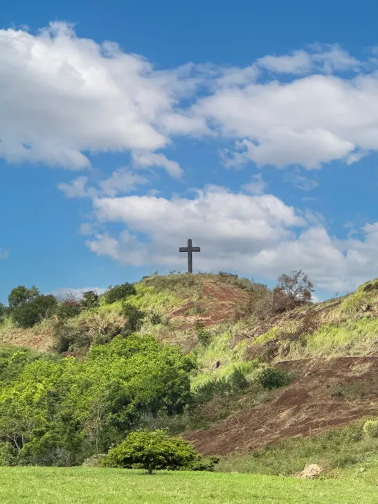 view of hill with cross on top of it with blue sky and white clouds