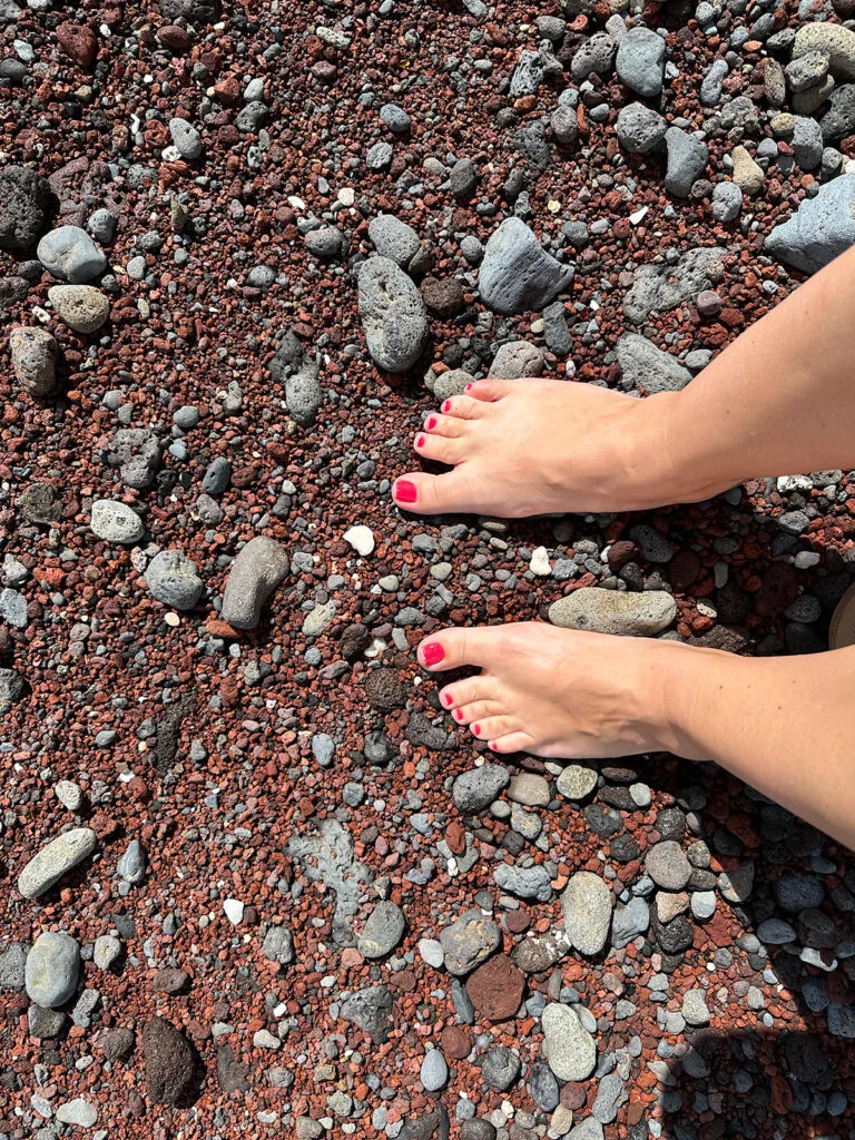 feet and legs standing on red sand beach with black rocks best things to do in Hana maui