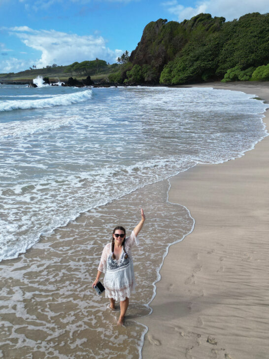 woman standing in water on sand with beach and coast in background