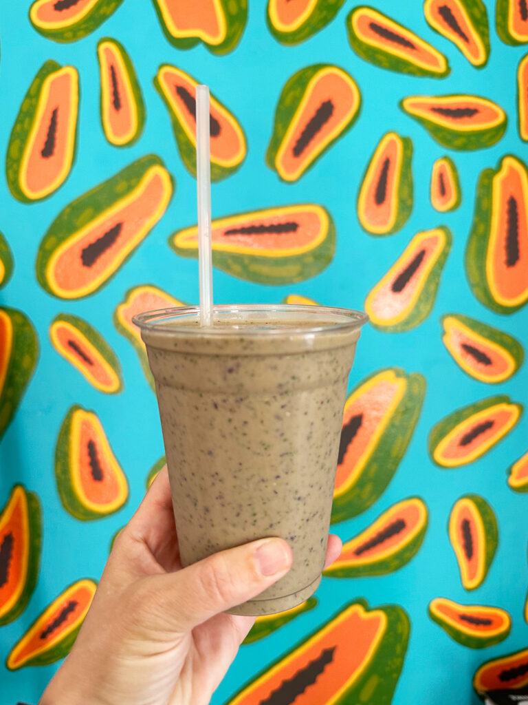 hand holding smoothie in cup against wallpaper with avocados