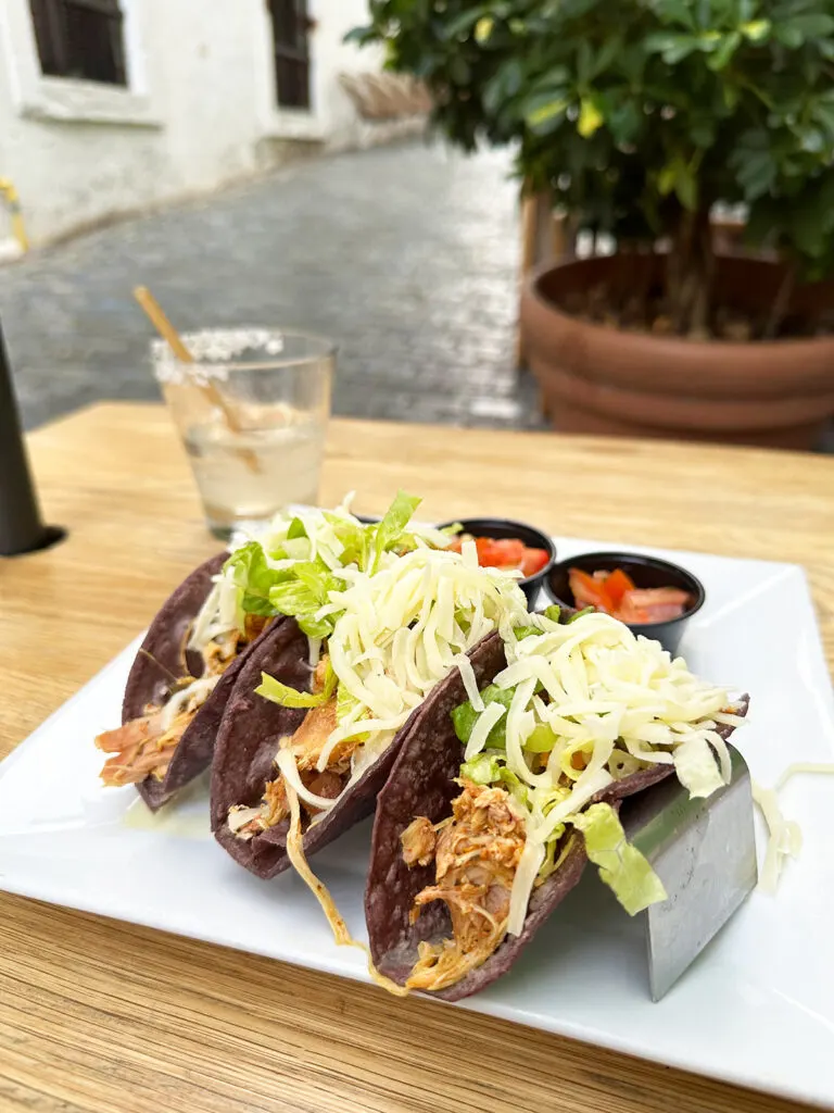 three tacos on plate with cheese and old San Juan street in distance