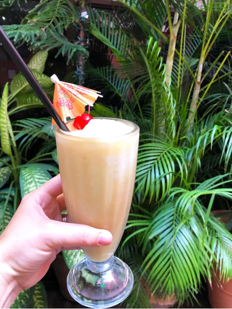 hand holding a Pina colada against a wall of tropical foliage in the best places to eat old San Juan