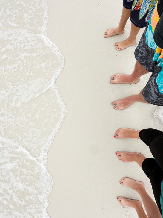 4 sets of feet on sandy ocean with wave on sand