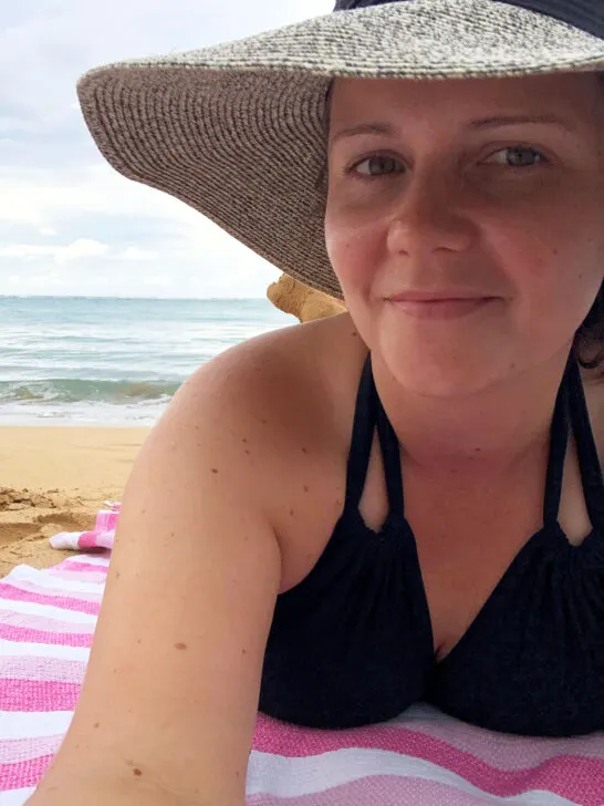 woman laying on beach towel with black swimsuit and beach hat