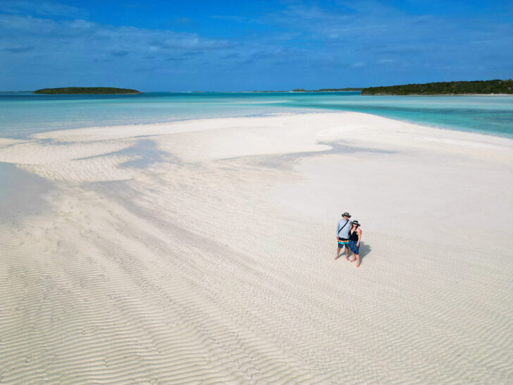 visit Exuma bahamas view of couple standing on sandbar with vivid Caribbean blue water in distance