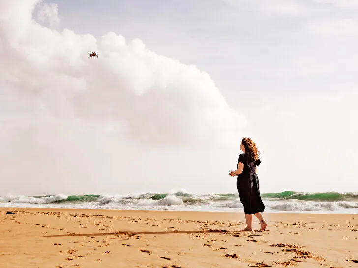 best travel drones view of woman in dress on beach flying a drone with waves in distance