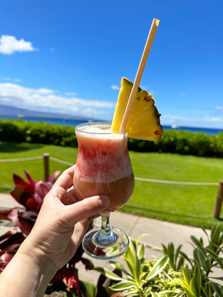 view of hand holding drink with ocean in distance