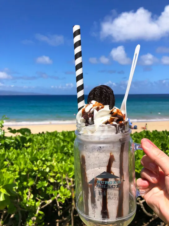 view of hand holding ice cream with straw Oreo and beach in distance