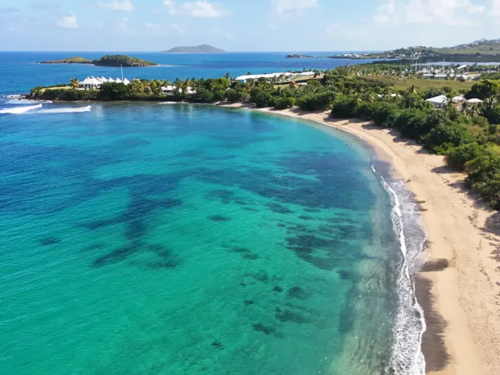 aerial view of bright blue water at shoys beach with crescent shaped beach and trees with hills in distance