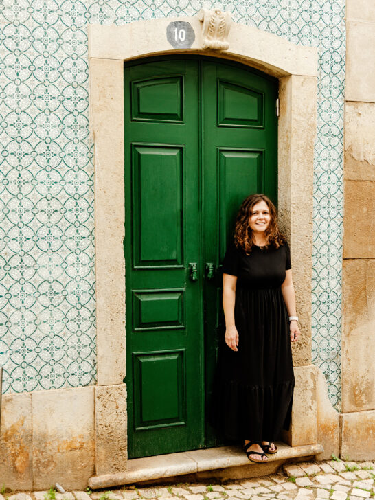 woman in black dress standing in front of green door with ornate tile