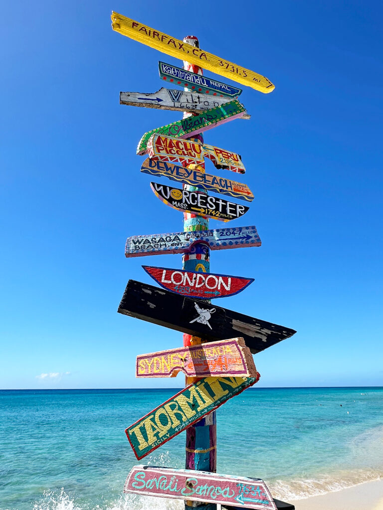 signs outside restaurant with cities and distances and beach in distance