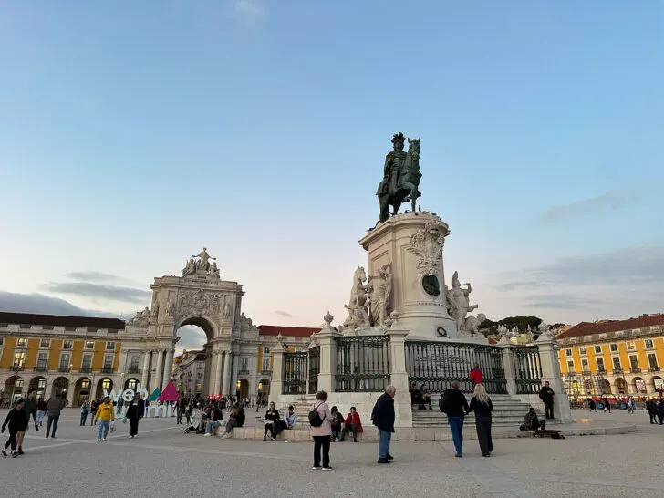 popular Lisbon square surrounded by people and large arch with statue in foreground