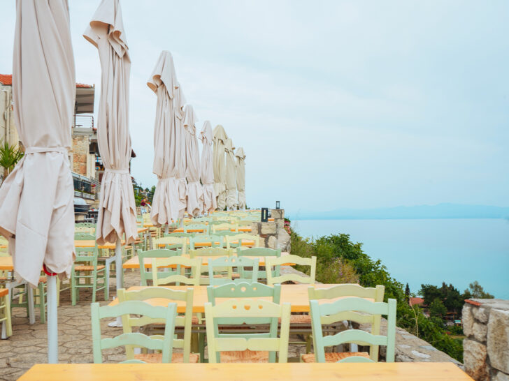 view of blue ocean at restaurant with orange and green tables and chairs with umbrellas in Afytos Greece