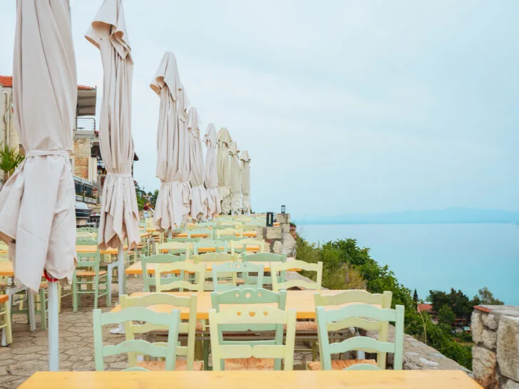 view of blue ocean at restaurant with orange and green tables and chairs with umbrellas in Afytos Greece
