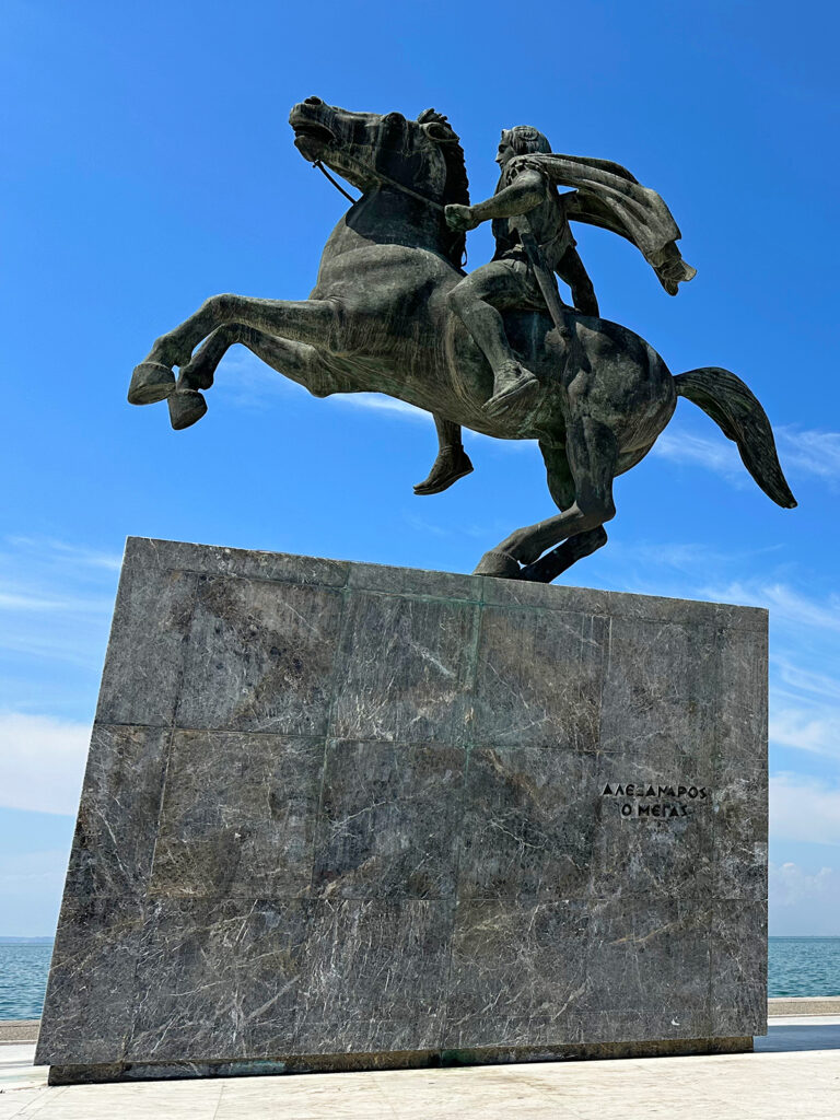 view of large Alexander the Great statue man riding horse on large square block greece travel itineraries