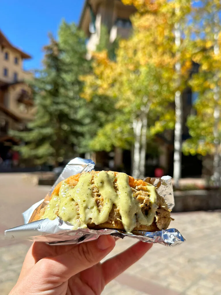 hand holding taco with dressing and yellow tree behind
