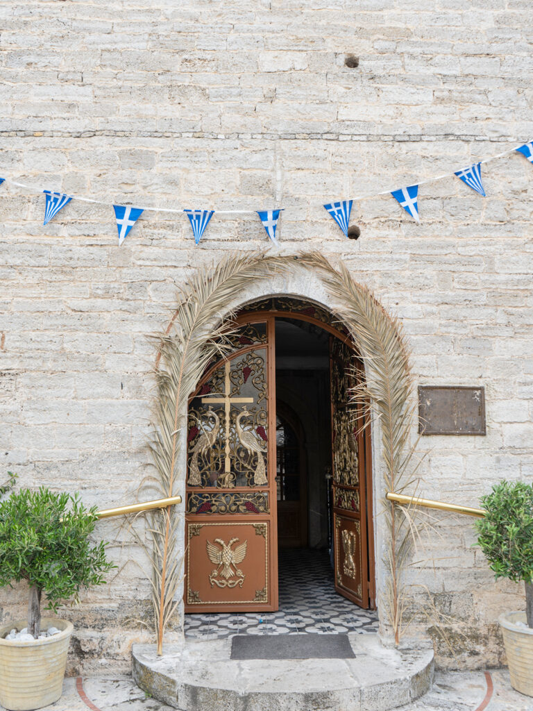 church door with greenery and greek flags on stone wall