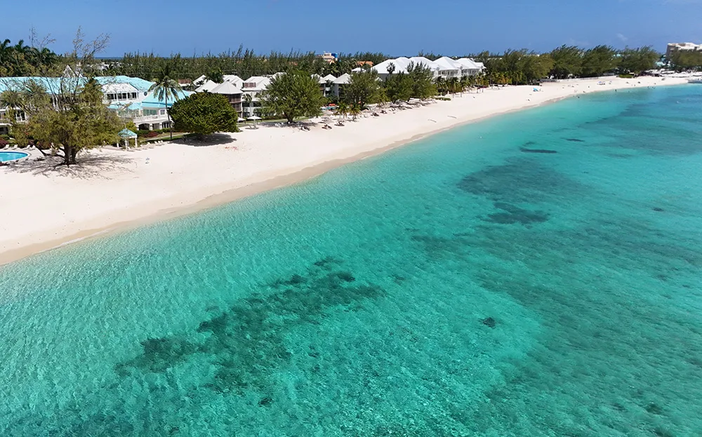 Cayman Islands travel guide view of teal beach white sand and trees and buildings in distance