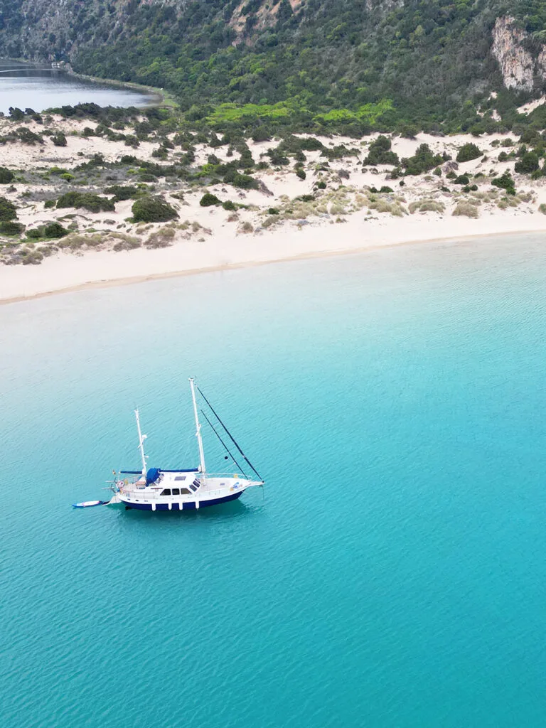 sailboat on blue water with sandy beach and cliff in distance Greece mainland itinerary