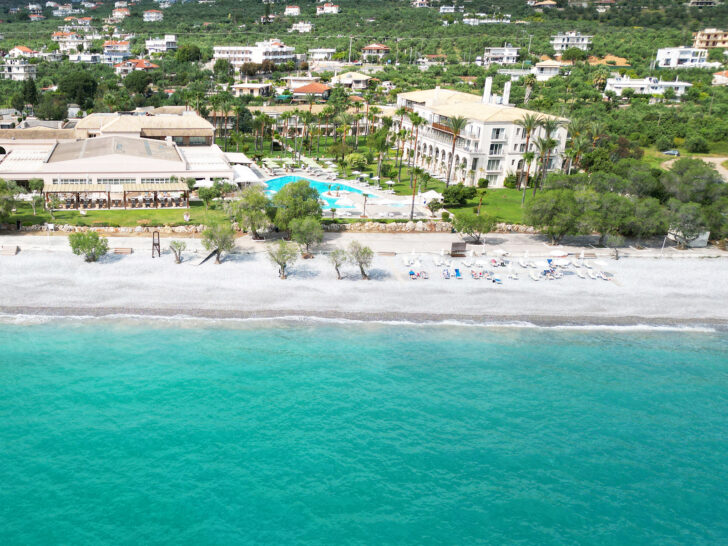 view of hotel and beach with bright teal water and pool with buildings best Greece itinerary
