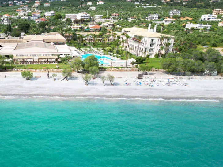 view of hotel and beach with bright teal water and pool with buildings best Greece itinerary