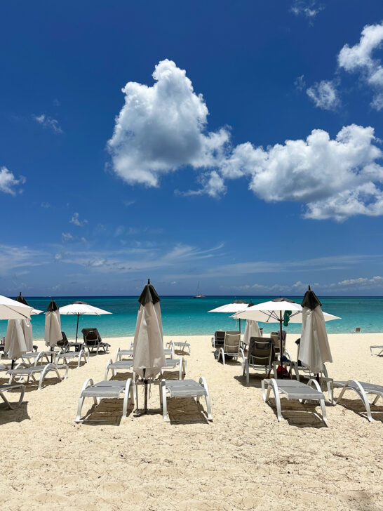 chairs and umbrellas sitting on beach with teal water in distance visiting Cayman Islands