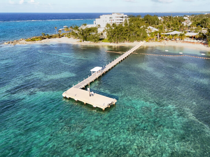 what to know before visiting the Cayman Islands view of pier with teal and blue water and island in distance