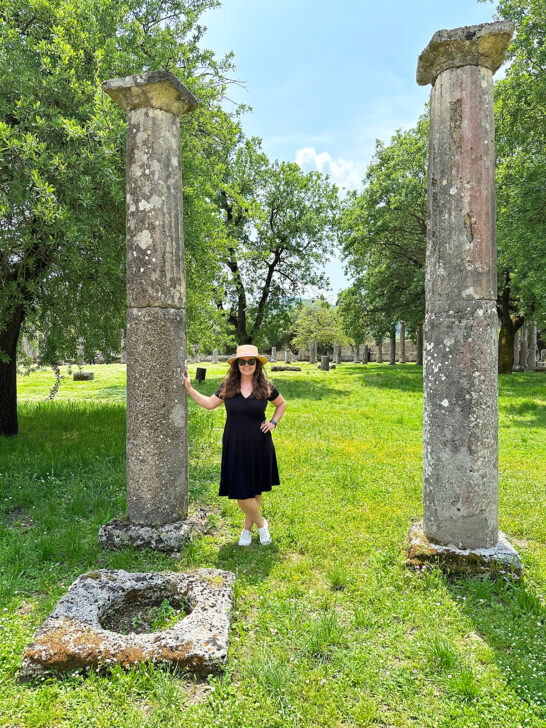 woman standing by page pillar in Ancient Olympia during a Greece mainland itinerary